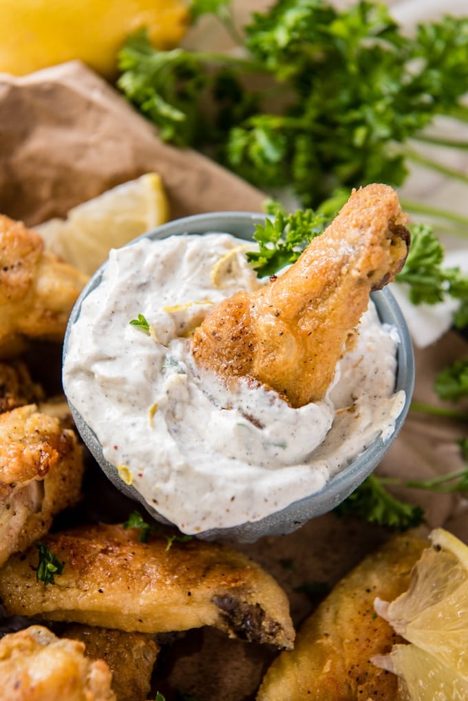 a crispy baked lemon pepper chicken wing in a bowl of yogurt dip