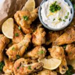 A plate full of chicken wings with lemon wedges and sauce