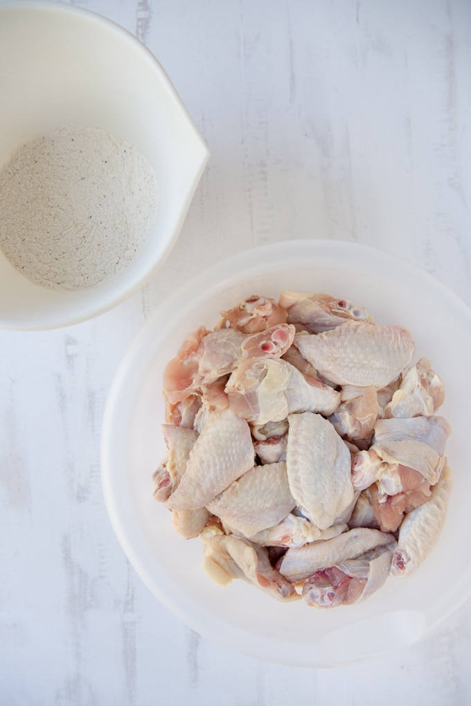 A bowl of chicken wings and a bowl of flour side by side