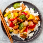 Sweet and sour pork over rice on a black plate.