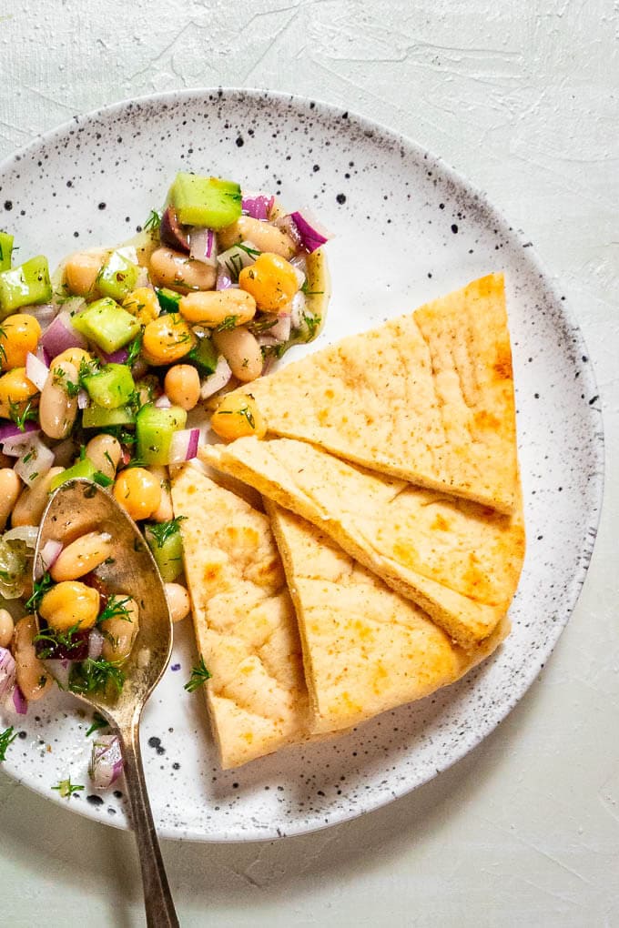 Bean salad on white plate with side of cut pita.