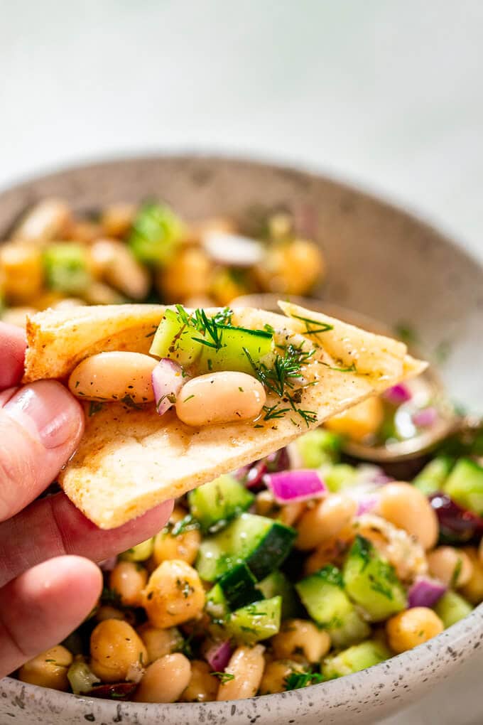 Holding a pita piece with beans, cucumber and dill.