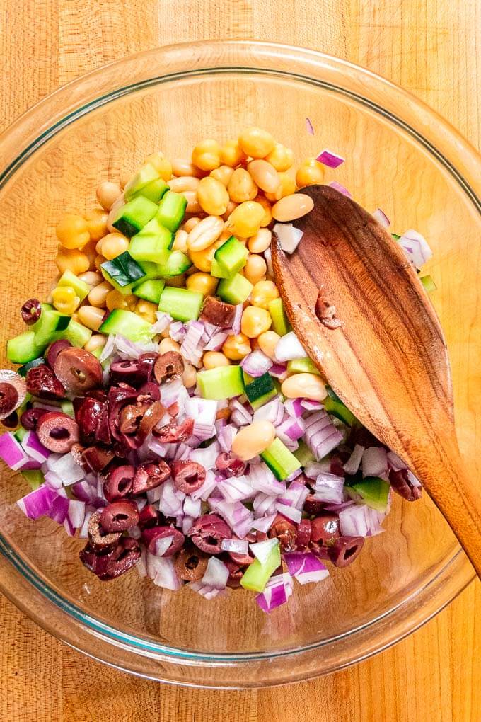 Glass bowl with beans, chopped cucumber, olives, and red onions.