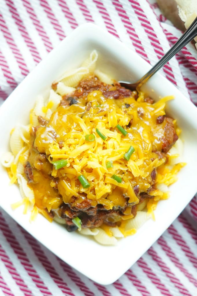 An overhead shot of pasta and chili topped with cheese in a white bowl.