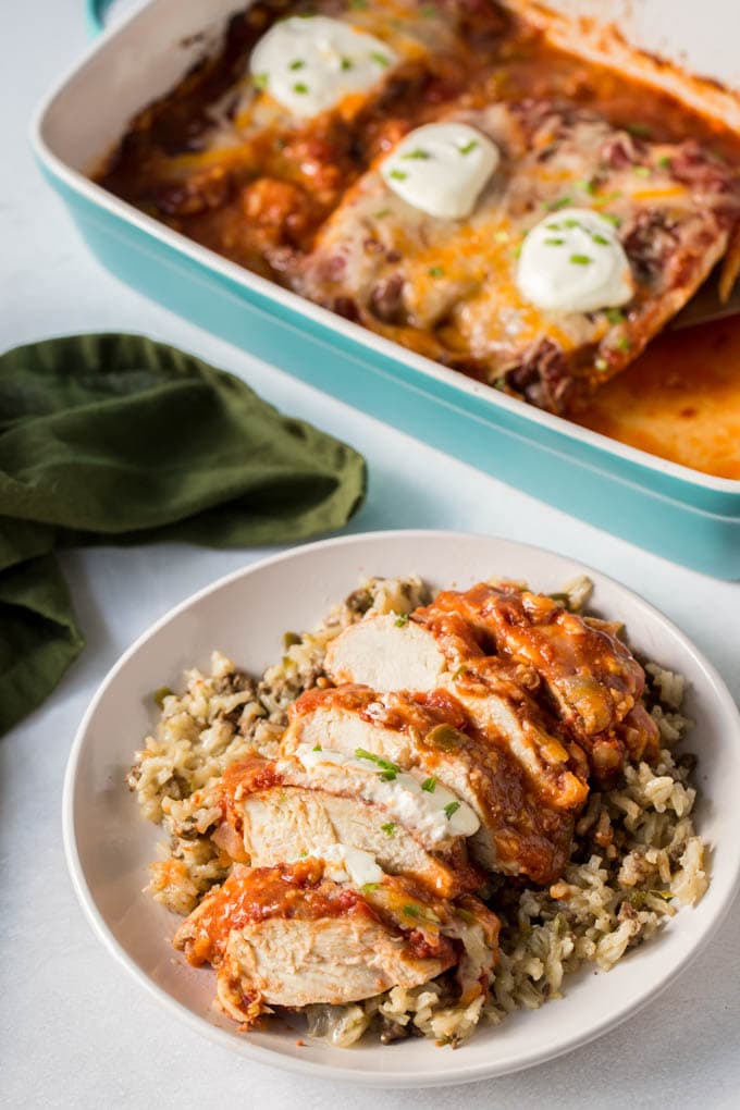 A pan with 3 chicken breasts covered with salsa and cheese and a plate with sliced chicken and rice