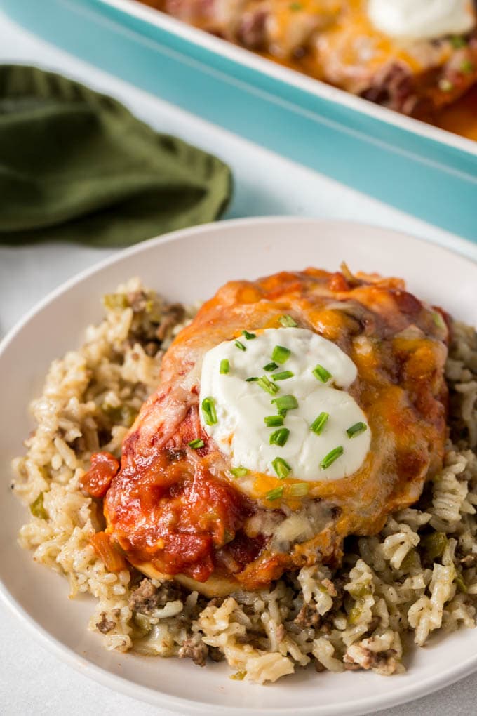 A whole chicken breast covered with salsa, cheese and sour cream on top of rice on a plate