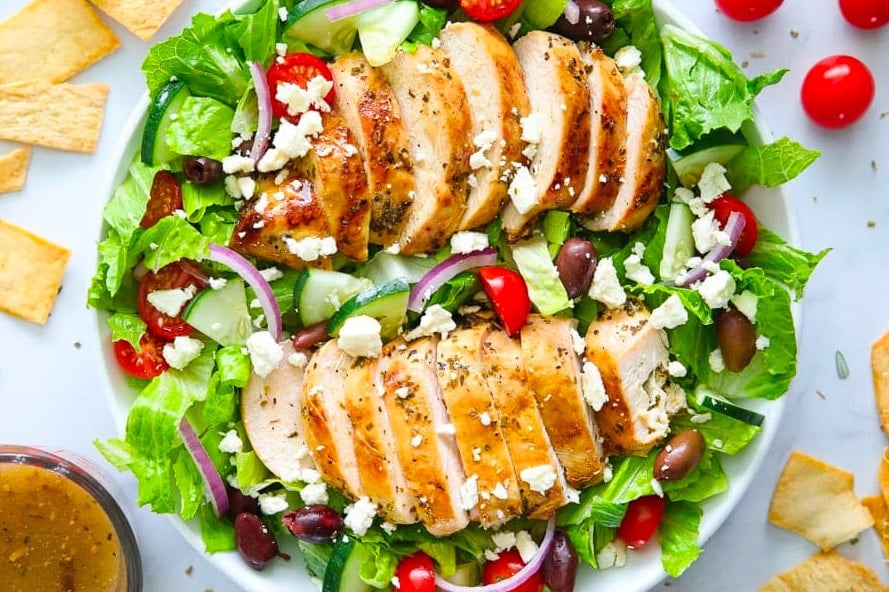 grilled chicken on a bed of lettuce with tomatoes and onions.