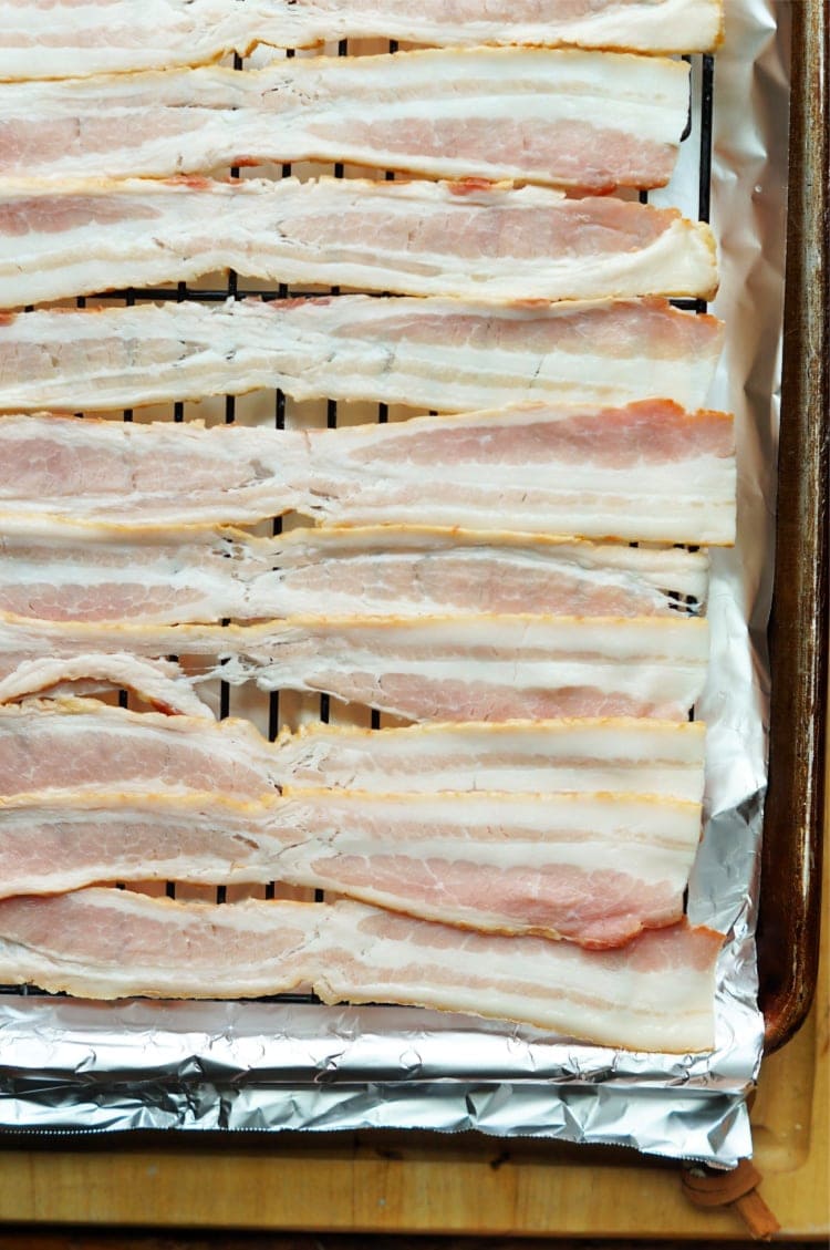 strips of raw bacon laid out on a cooling rack on top of a foil lined baking sheet.