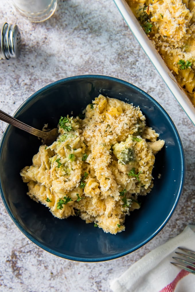 A blue bowl filled with chicken casserole with pasta and broccoli and cheese