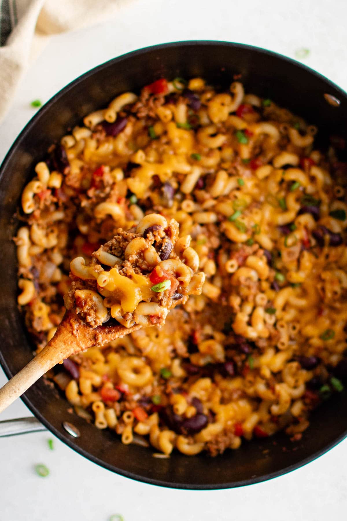 Chili and macaroni with cheese in a skillet; a wooden spoon.