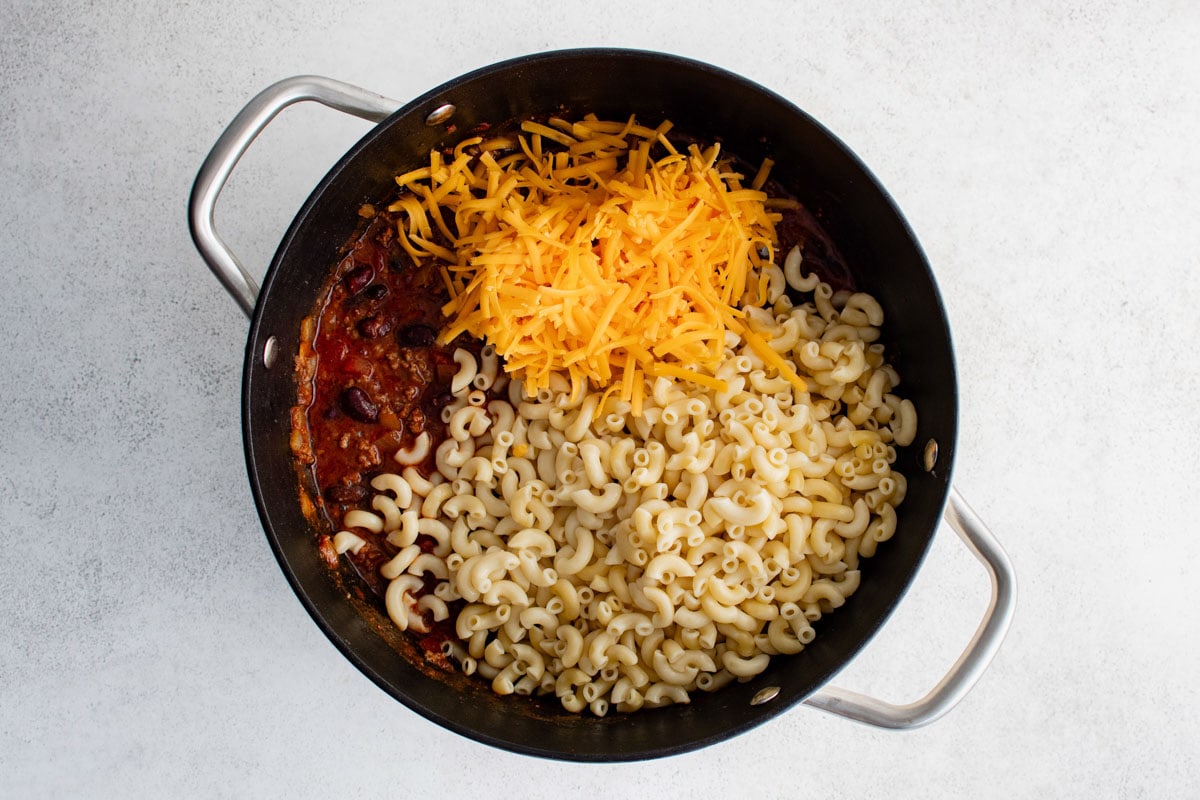 Chili, macaroni and shredded cheese in a pot.