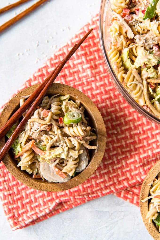 Chicken, pasta and vegetable in a small bowl with asian dressing and chopsticks.
