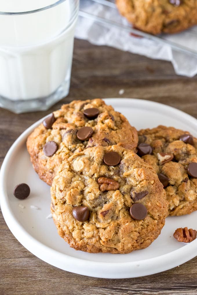 A plate of 3 soft, chewy cowboy cookies with a glass of milk. 