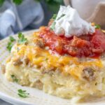 A plate of egg and hashbrown casserole with sausage, cheese, salsa, and sour cream.