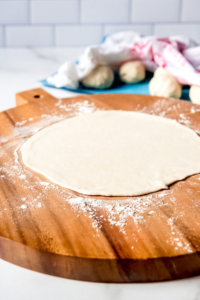 An image of tortilla dough rolled out into a flat circle on a cutting board.