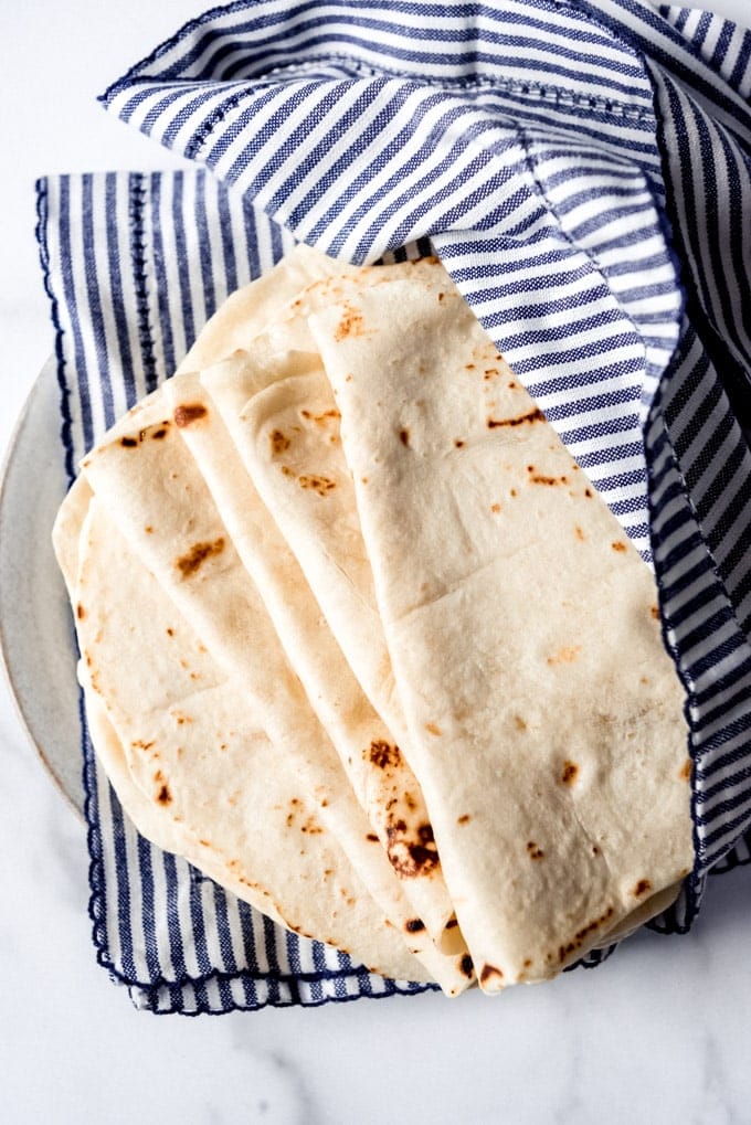 a stack of fresh homemade flour totillas sitting on a blue striped towel.