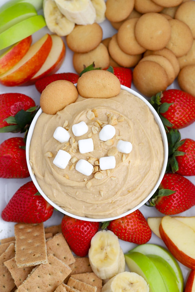 Fluffernutter peanut butter dip topped in a white bowl surrounded by fruit. 