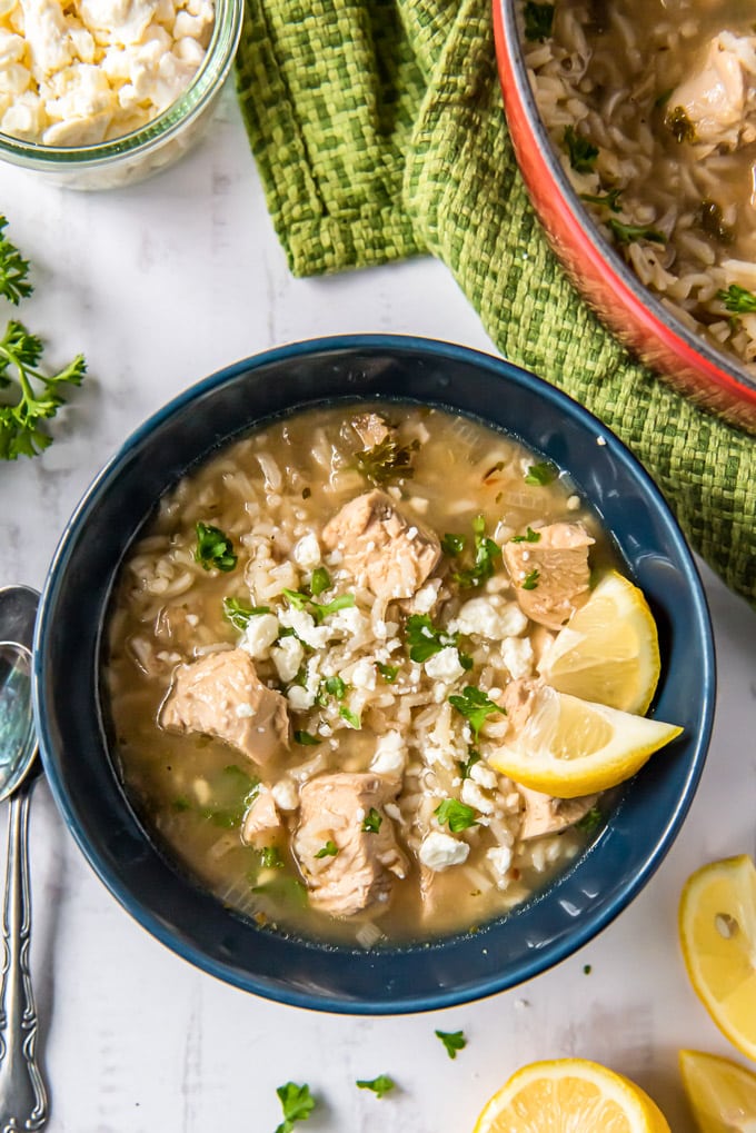 A bowl of Greek Lemon Chicken Soup with feta cheese, parsley and lemon wedges.