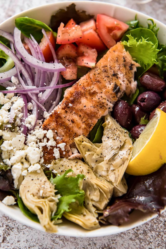 A close up image of a bowl of salad with salmon, artichokes, tomatoes and olives