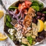 A bowl of salad with salmon, red onions, and olives