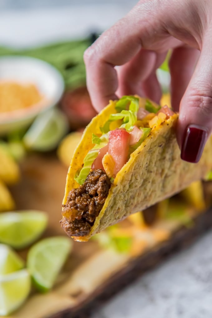 A hand holding a taco filled with ground beef, lettuce, cheese and tomatoes