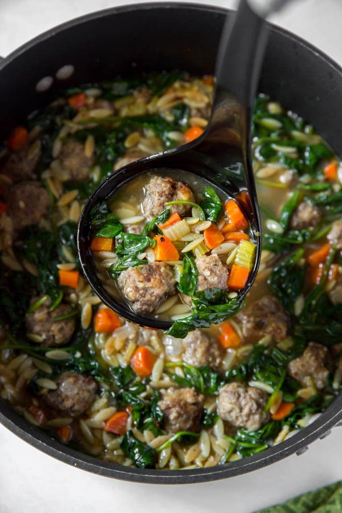 A ladle of Soup with meatballs, spinach, carrots and orzo.