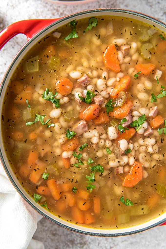 A large soup pot filled with navy bean soup with ham, carrots and celery