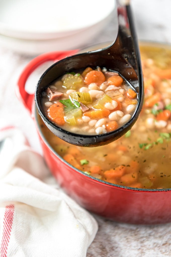 a black ladle with white beans, broth, ham and carrots