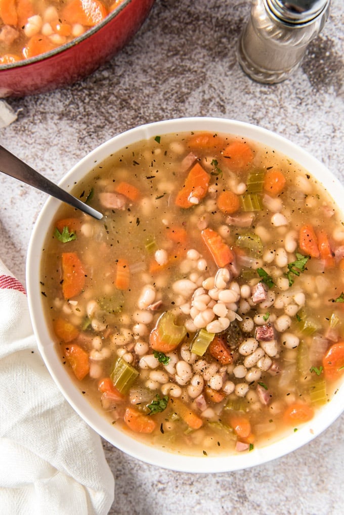 a white bowl filled with beans, carrots and ham soup.