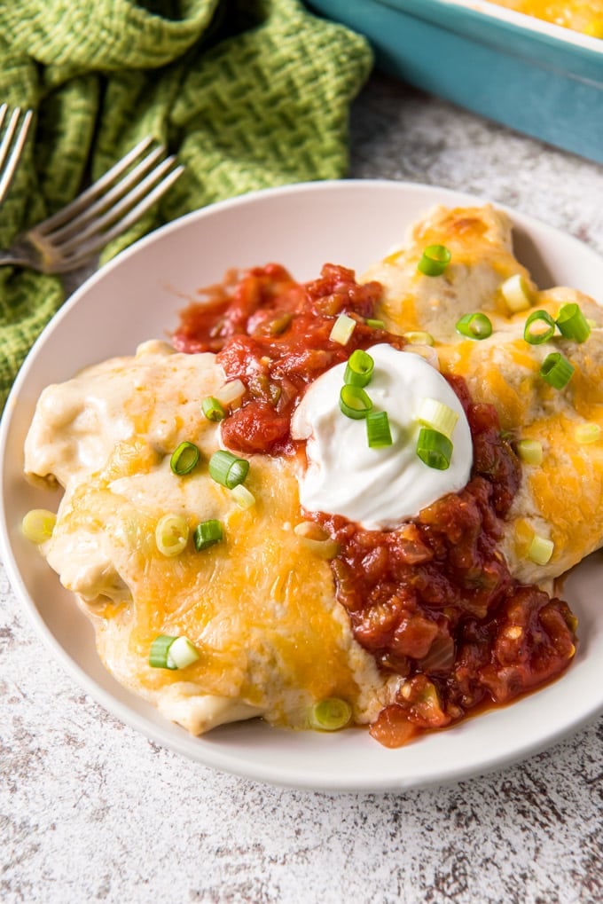 A close up of two chicken enchiladas on a plate with sour cream and salsa