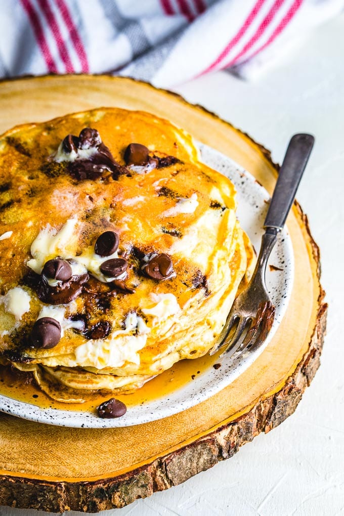 Chocolate chip pancakes with butter and syrup in white plate on wooden board.