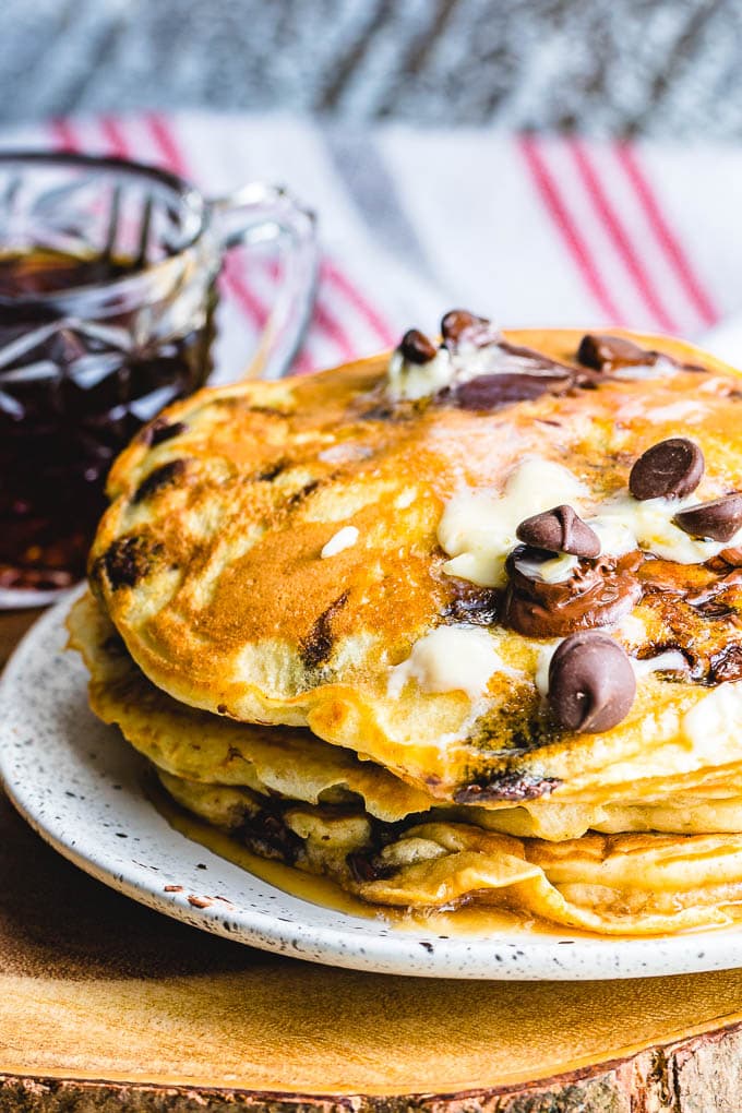 Chocolate chip pancakes in white plate with syrup in background.