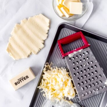 A stick of butter, cheese grater, and grated butter