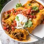 A close up of Beef Enchiladas topped with sour cream, salsa, and cilantro