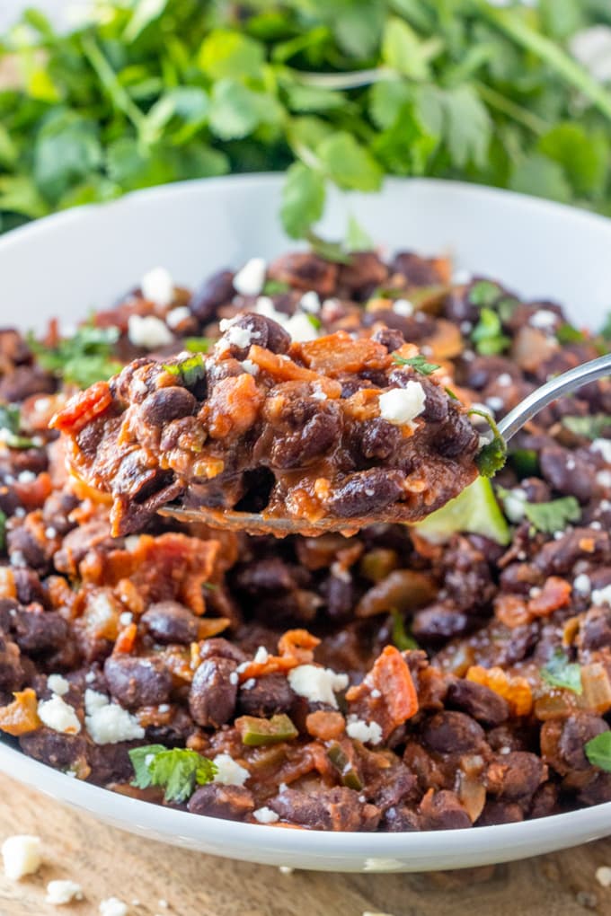 Black beans with salsa and bacon in a large dish with a spoon lifting up a serving.