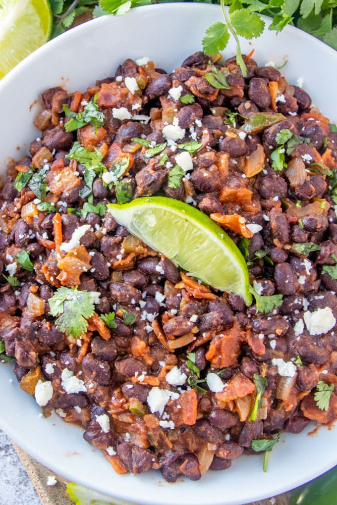 an overhead image of a large bowl of mexican black beans with a slice of lime