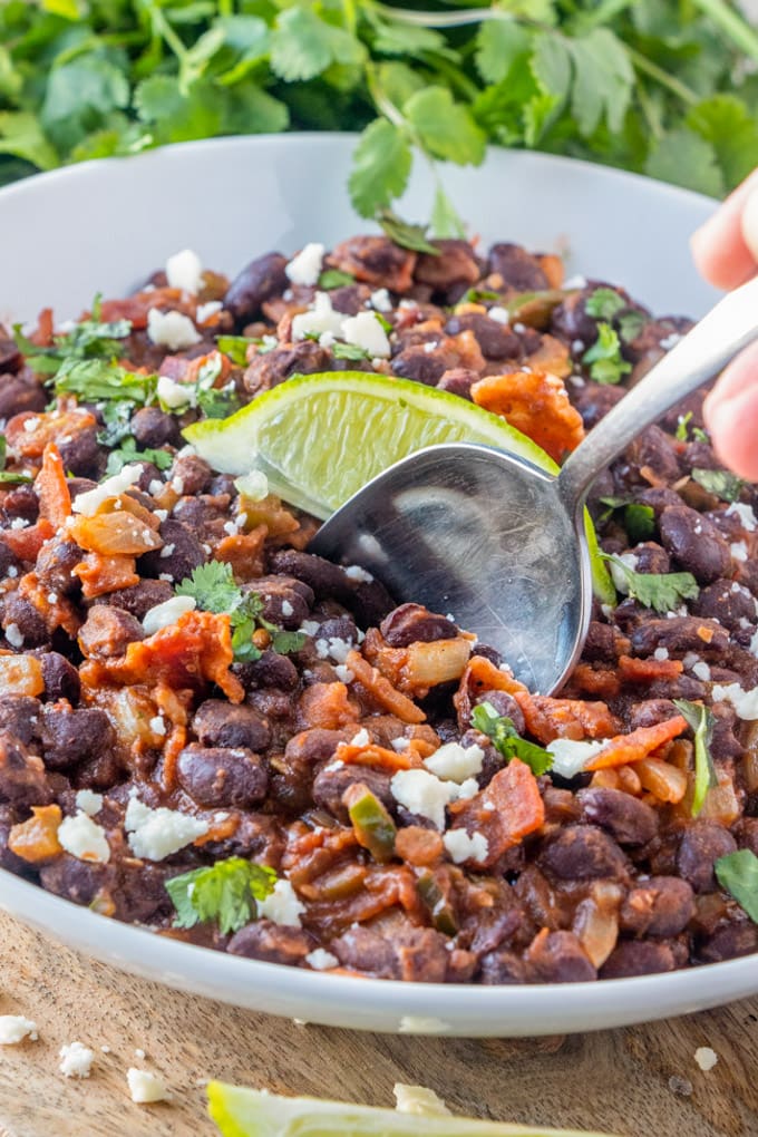 a large bowl of mexican black beans with a spoon and a lime slice.