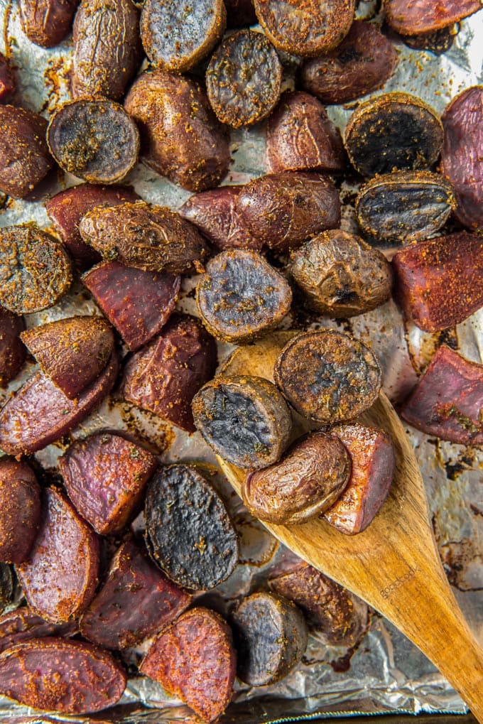 A sheet pan covered with foil with roasted cut up purple potatoes and a wooden spoon