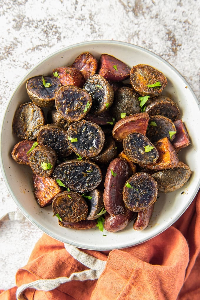 a white bowl full of roasted purple potatoes sitting next to an orange towel