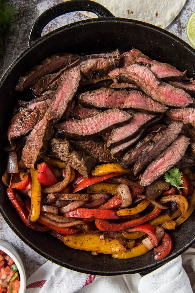 Uma frigideira de ferro fundido com bife fatiado, pimentão e cebola.