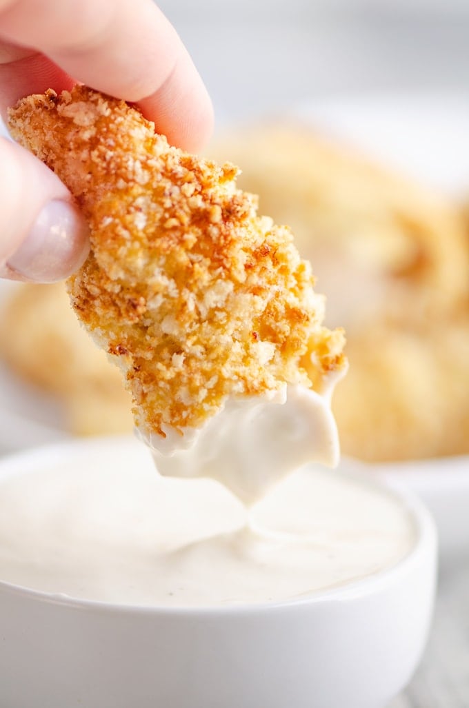 A hand dipping a Chicken Tender in a bowl of ranch dressing
