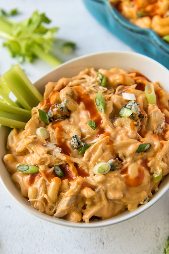 a bowl of buffalo chicken mac and cheese with blue cheese, green onions and celery sticks