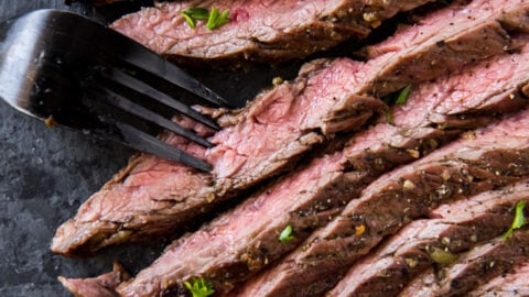 carne asada steak sliced on a black cutting board with a fork.