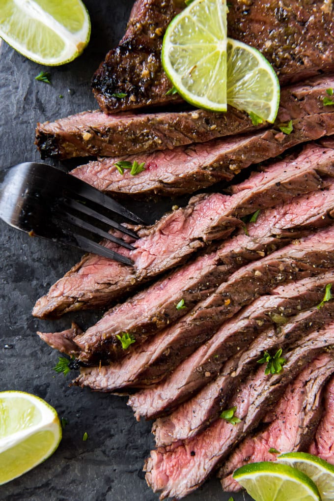 carne asada steak sliced on a black cutting board with a fork.