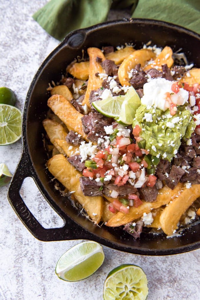 a large cast iron skillet with french fries, steak, guacamole and cheese