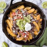 Cast iron pan filled with fries and topped with carne asada, quacamole, salsa, and sour cream.
