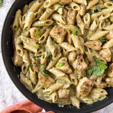 A skillet with pasta and chicken in a creamy pesto sauce