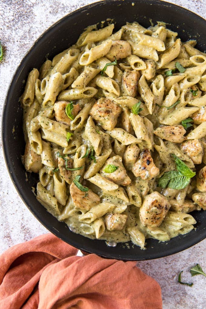 A skillet with pasta and chicken in a creamy pesto sauce