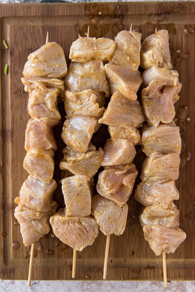 raw chicken breast chunks in marinade and threaded on wooden skewers.