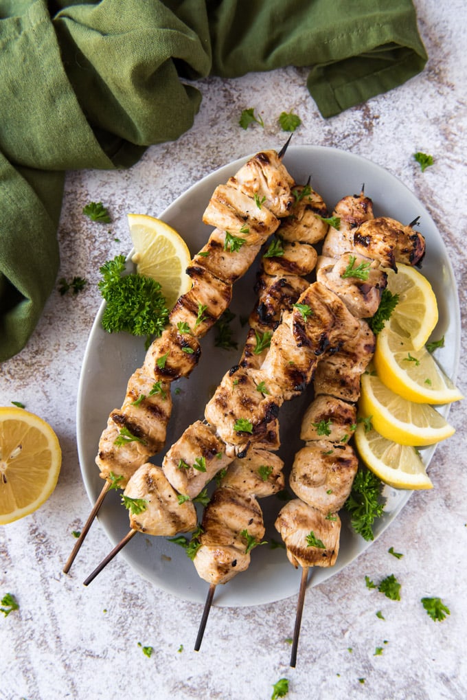 cut up chunks of chicken on skewers, grilled, with lemon on a plate